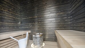 Una sala de sauna con paredes de madera, bancos y un recipiente de vidrio con piedras.