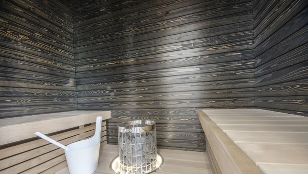 A sauna room with wooden walls, benches, and a glass container with rocks. - Vanha Postitalo (Varkaus)