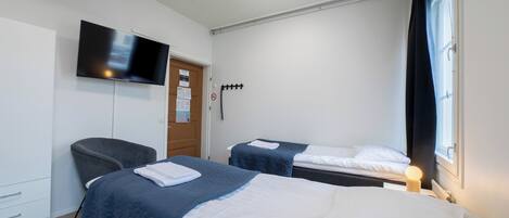 Ein Hotelzimmer mit zwei Betten, einem wandmontierten Flachbildfernseher, einem Schreibtisch mit Stuhl und einem Fenster mit Vorhängen.