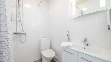 A modern bathroom with white tiles, a toilet, a shower, and a sink with a mirror above it.
