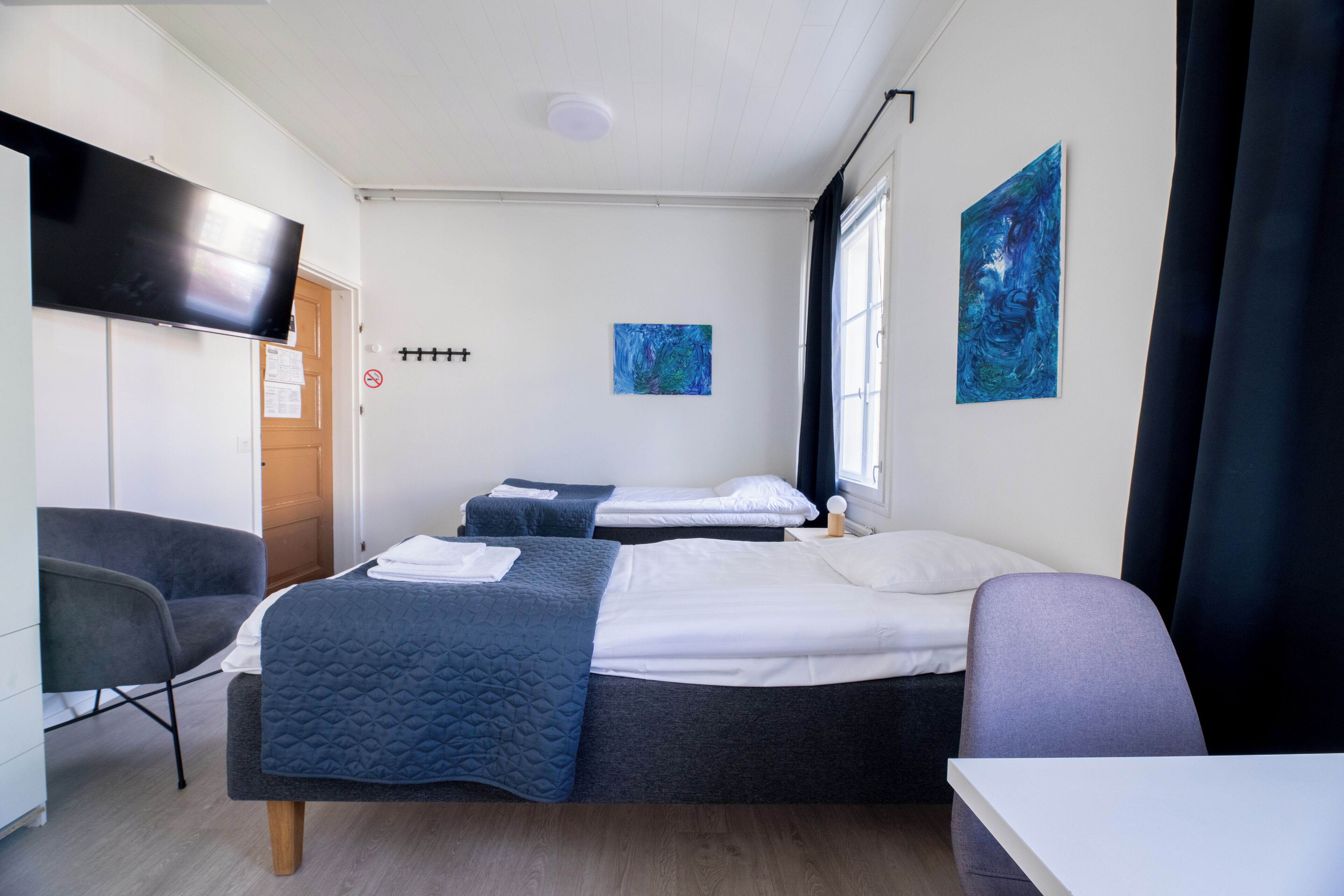 Ein Hotelzimmer mit zwei Betten, einem Schreibtisch, einem Stuhl, einem Fernseher und Bildern an den Wänden.