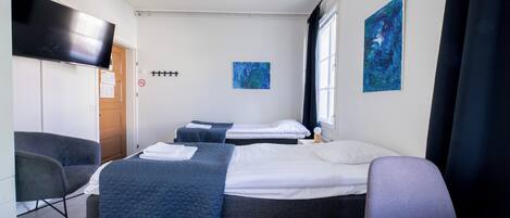 A hotel room with two beds, a desk, a chair, a TV, and artwork on the walls.