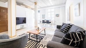 A modern living room with a sofa, a coffee table, and a TV. There is a dining area with chairs and a table in the background. - Vanha Postitalo (Varkaus)