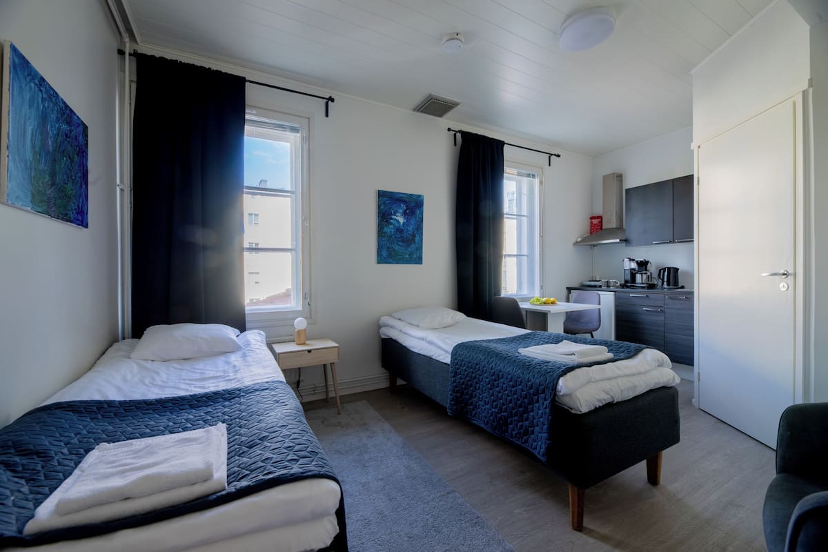 Una habitación de hotel moderna con dos camas individuales, un escritorio pequeño, kitchenette y televisión.