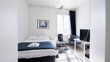 A hotel room with a bed, a desk, a chair, a television, and a window with curtains.