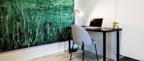 A modern office space with a laptop on a desk, a chair, a lamp, and a large abstract painting on the wall.