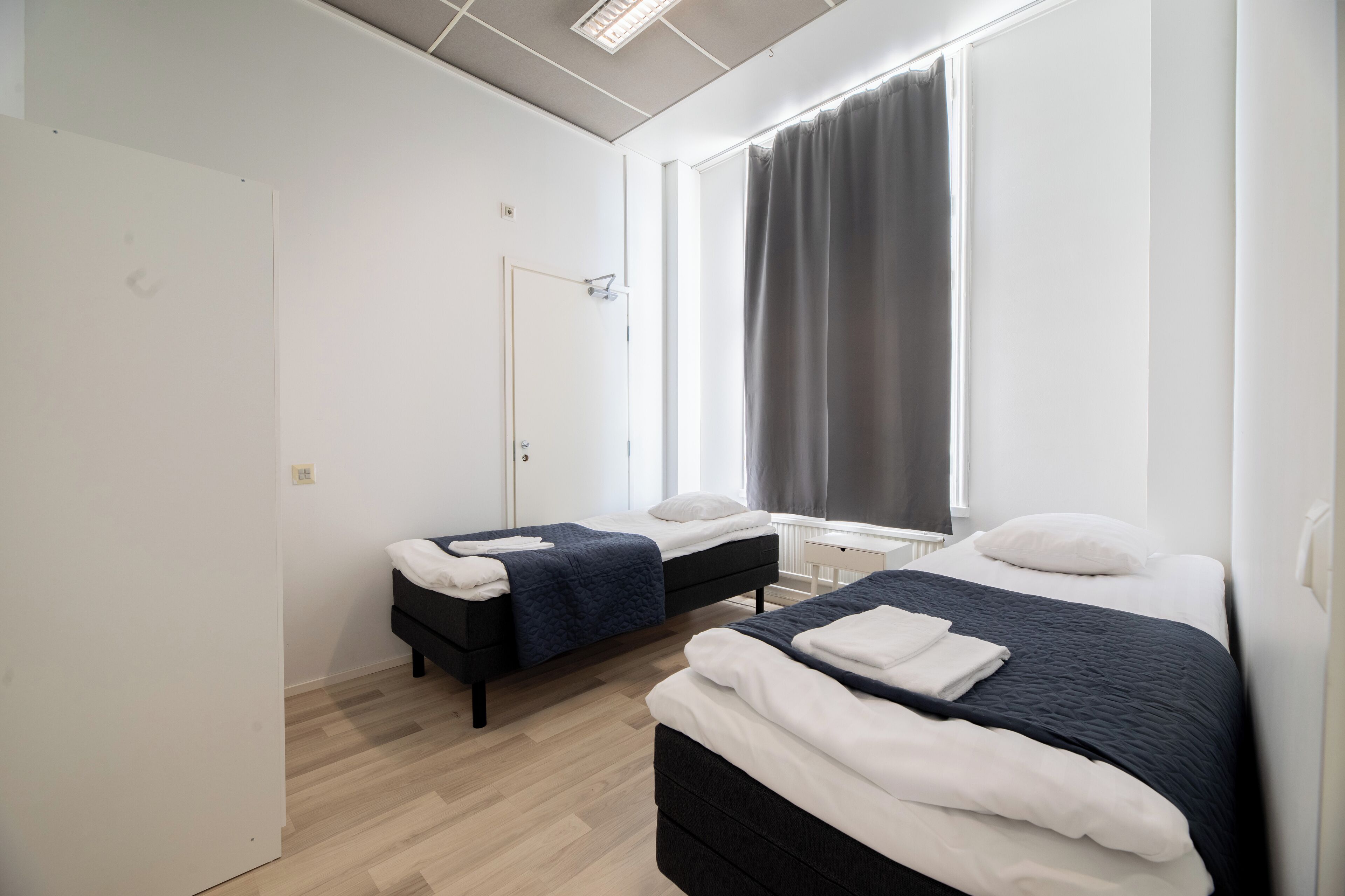 Ein modernes Schlafzimmer mit zwei Betten, einem Fenster mit Vorhängen und einem weißen Heizkörper.