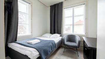Un dormitorio con una cama, una silla, un escritorio y dos ventanas.