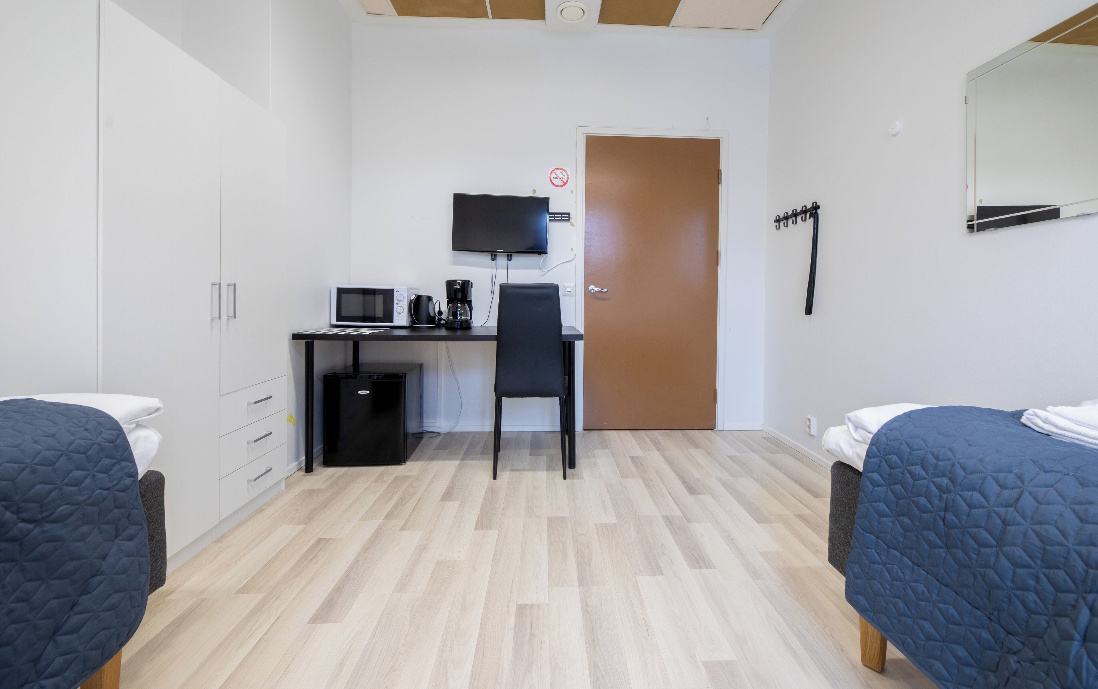 Habitación de hotel con dos camas, un escritorio con computadora, televisión y una puerta con letrero.