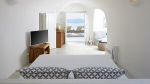 Une chambre moderne avec un grand lit, une télévision et une vue sur la mer, visible à travers une porte ouverte.