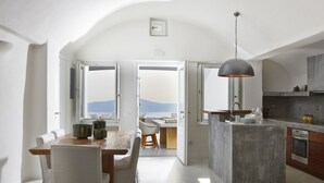 Une cuisine moderne avec un îlot central, un coin repas comprenant une table et des chaises, et une vue dégagée grâce aux portes ouvertes.