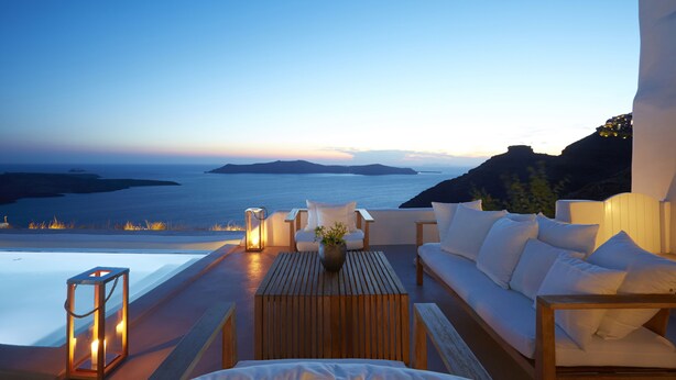 Une terrasse avec une table en bois, un canapé blanc et une vue sur la mer au crépuscule.