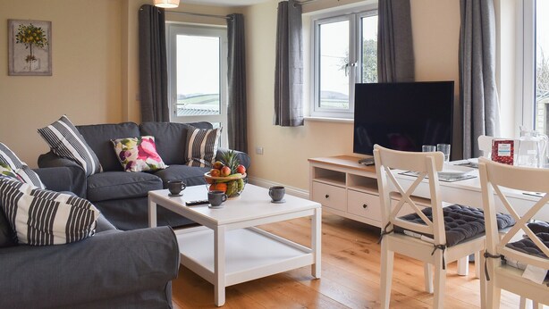 Ett modernt vardagsrum med en soffa, ett soffbord och en tv. Det finns gardiner, ett fönster och en tavla på väggen.