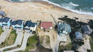 Vista aérea de una zona residencial costera con casas, una playa y olas del océano.