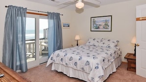 A bedroom with a bed, two bedside lamps, a ceiling fan, and a view of the ocean through a sliding door. - Starlights Condos, OCEANFRONT, Extraordinary View, Together Yet Private! (Buxton)