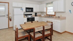 A compact kitchen with white cabinets, a microwave, stove, and a coffee maker. There is a wooden dining table with chairs. - Starlights Condos, OCEANFRONT, Extraordinary View, Together Yet Private! (Buxton)
