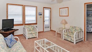 A living room with a sofa, two armchairs, a coffee table, a television, and a door with a picture frame. - Starlights Condos, OCEANFRONT, Extraordinary View, Together Yet Private! (Buxton)