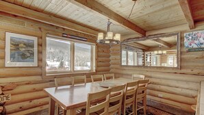 A log cabin interior with a wooden dining table and chairs, large windows, and a mirror on the wall. - Cook Family Lodge (Breckenridge)