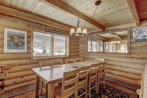 Ein rustikales Blockhaus-Interieur mit einem Holzespeisetisch und -stühlen, großen Fenstern und einem Spiegel an der Wand.