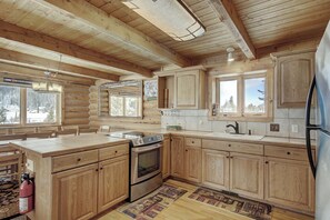 A log cabin interior with a kitchen, dining area, and a fireplace.