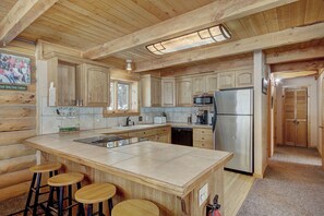 Eine Blockhausküche mit Holzausstattung, einem Edelstahlkühlschrank, einem Geschirrspüler und einer Bar mit Hockern.