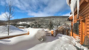 A wooden cabin with a snow-covered deck and a view of a forested mountain. - Cook Family Lodge (Breckenridge)