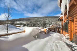 A wooden cabin with a snow-covered deck and a view of a forested mountain. - Cook Family Lodge (Breckenridge)