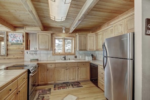 A kitchen with wooden cabinets, a stainless steel refrigerator, and a window with a view of trees.