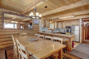 A wooden cabin interior with a dining area, kitchen, and a large mirror reflecting the room.
