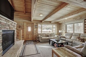 A log cabin interior with a fireplace, two sofas, a coffee table, and a large window offering a view of a snowy landscape. - Cook Family Lodge (Breckenridge)