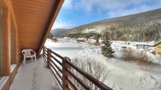 A wooden balcony with a white plastic chair, overlooking a snowy landscape with houses and a forested mountain. - Cook Family Lodge (Breckenridge)