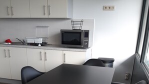 Una cocina moderna con armarios blancos, una encimera negra y un microondas. Hay una mesa de comedor con sillas negras y una ventana que proporciona luz natural.