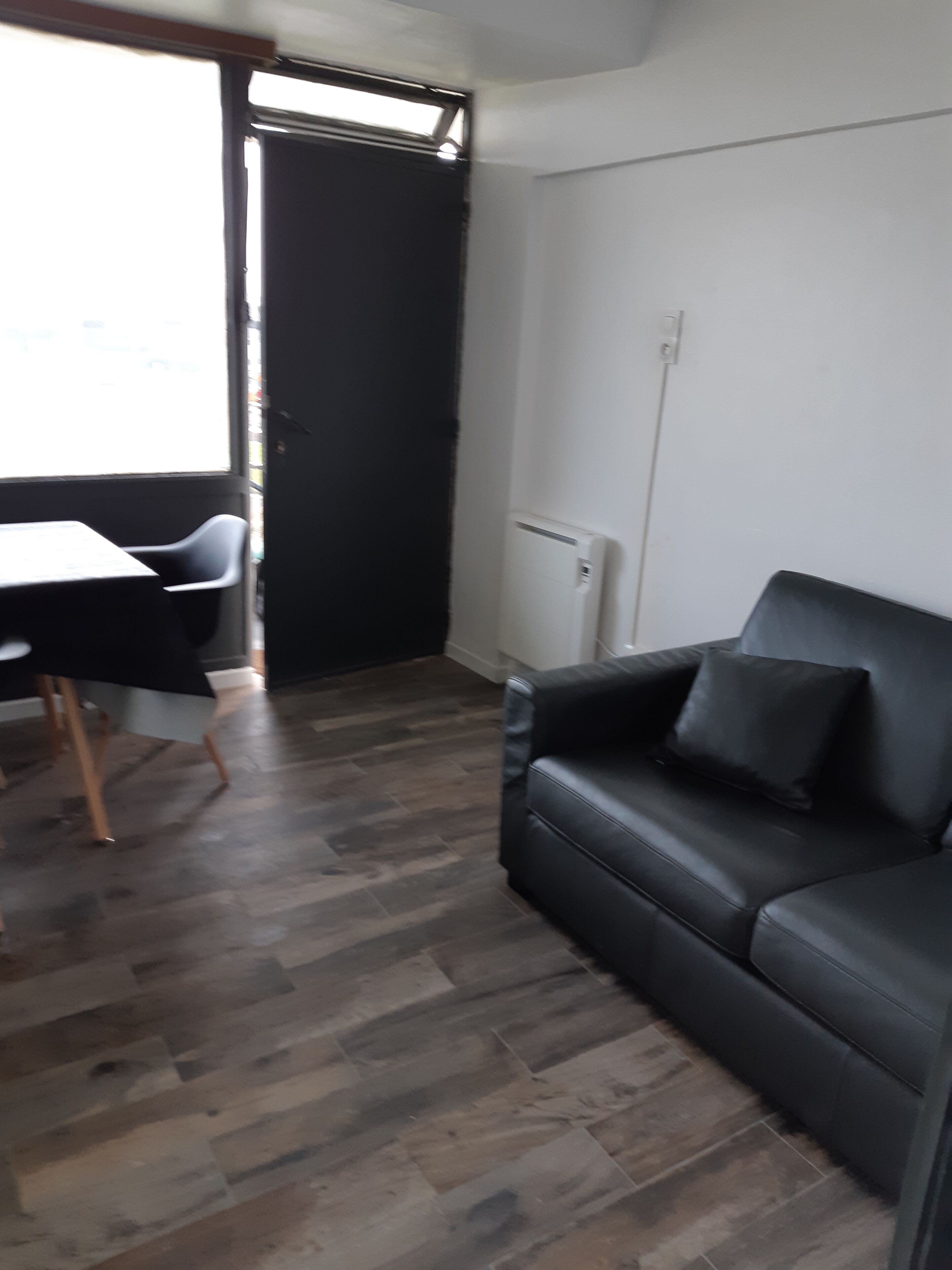 Een kamer met een zwarte leren bank, een eettafel met stoelen en een groot raam.