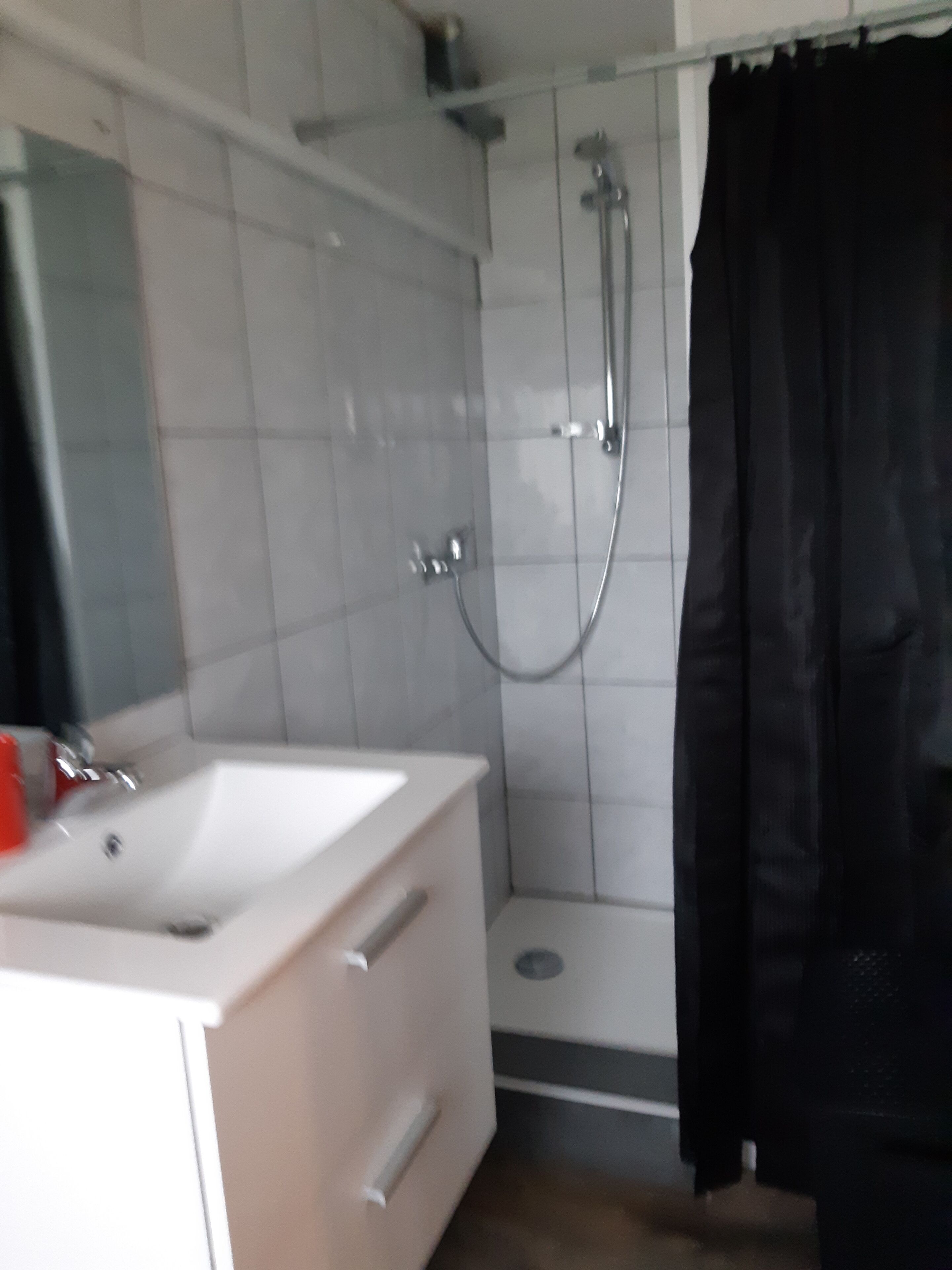 A bathroom with a white sink, a shower, and a black curtain.