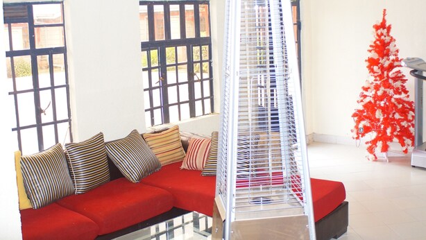 A red sofa with striped cushions, a metal ladder, and a red artificial tree in a bright room with large windows. - Bells Guest House (Ol Kalou)
