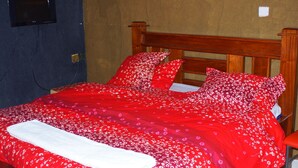 A bed with a red floral bedspread and matching pillows, a wooden headboard, and a white blanket. - Bells Guest House (Ol Kalou)