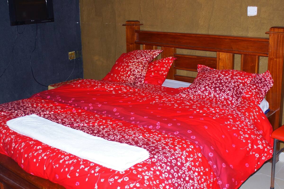 A bed with a red floral bedspread and matching pillows, a wooden headboard, and a white blanket.