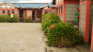 A building with a red facade, a paved entrance, and a potted plant in the foreground. - Bells Guest House (Ol Kalou)