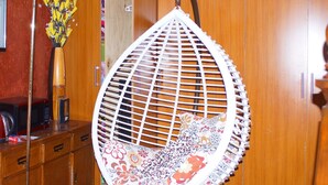 A hanging chair with a floral pattern, a wooden cabinet with drawers, and a vase with yellow flowers. - Bells Guest House (Ol Kalou)