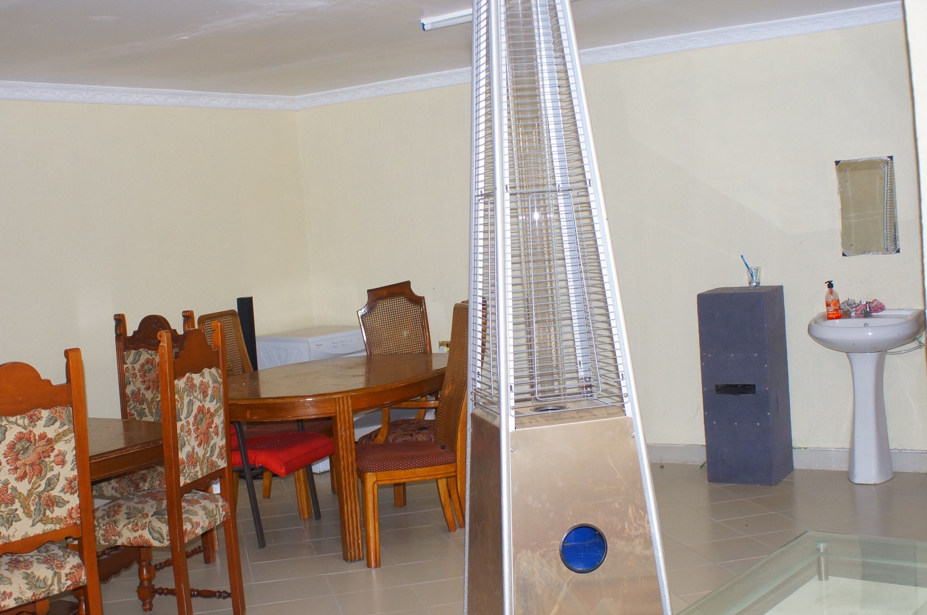 A dining area with a wooden table and chairs, a tall, narrow air conditioning unit, and a pedestal sink.