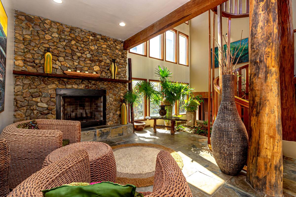 A cozy interior with a stone wall, a fireplace, wicker furniture, and a large vase.