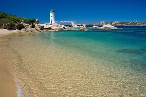 A clear beach with a lighthouse, rocky shoreline, and calm sea.
