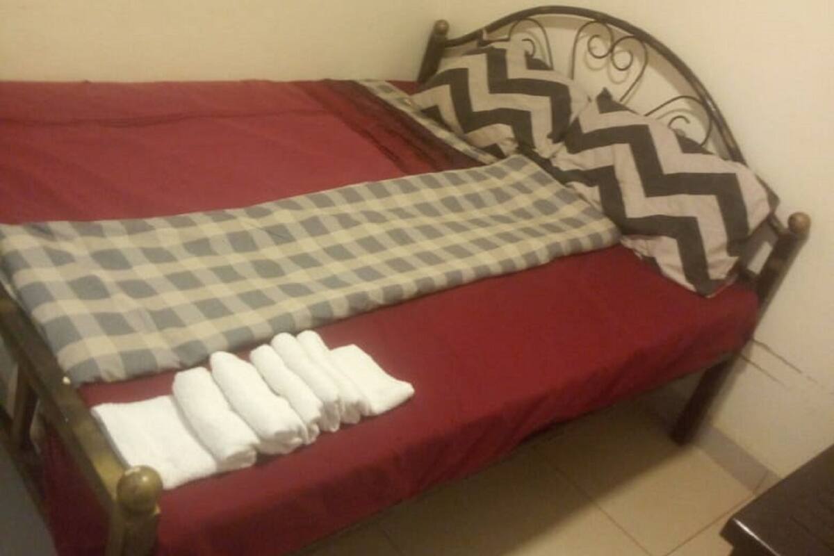 Un lit simple avec une couverture rouge, un oreiller à carreaux et des serviettes blanches soigneusement pliées.