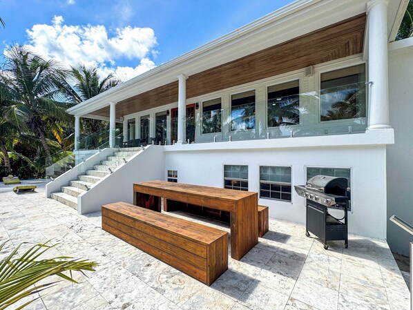 Una casa moderna de dos pisos con terraza de madera, mobiliario exterior y una parrilla.