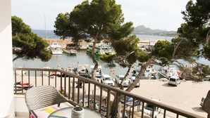 A balcony with wicker furniture, a glass table, and a view of boats and trees. - Front line apartment (Cala Rajada)