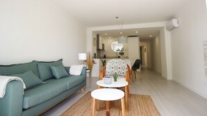 A living room with a sofa, a dining table, and a kitchen in the background. - Front line apartment (Cala Rajada)