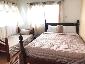 A bedroom with two single beds, a wooden headboard, and a large window with curtains.