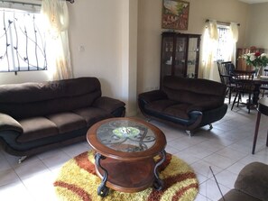 A living room with two sofas, a glass coffee table, and a dining area with chairs and a table.