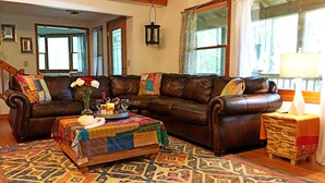 A cozy living room with a brown leather sofa, a colorful rug, and a small wooden table with a vase of flowers. - Yoga & Peaceful, Elegant, Bohemian Vibes Surrounded by Forest (Blairsville)