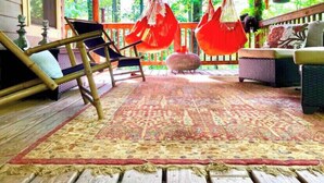 A wooden porch with hanging red fabric chairs, a patterned rug, and a wicker sofa. - Yoga & Peaceful, Elegant, Bohemian Vibes Surrounded by Forest (Blairsville)